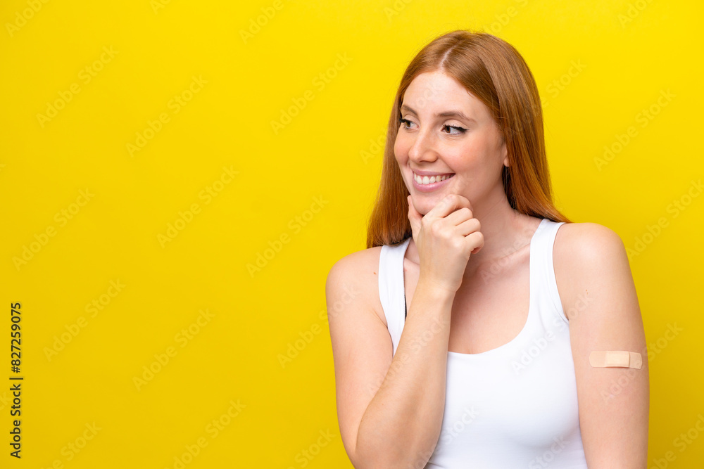 Young redhead woman wearing a band-aids isolated on yellow background thinking an idea and looking side Young redhead woman wearing a band-aids isolated on yellow background thinking an idea and looking side