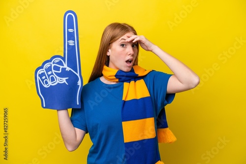 Young redhead sports fan woman isolated on yellow background doing surprise gesture while looking to the side