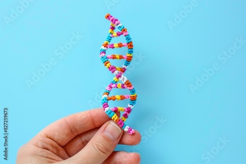 Hand holding a colorful DNA model against a plain blue background, highlighting simplicity and creativity in genetic education