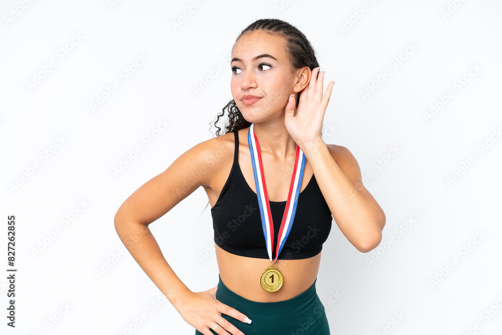 Young sport woman with medals isolated on white background listening to something by putting hand on the ear Young sport woman with medals isolated on white background listening to something by putting hand on the ear