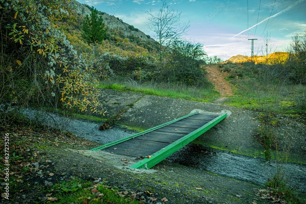 Handcrafted bridge over a stream leading to a river on a sunny day Handcrafted bridge over a stream leading to a river on a sunny day