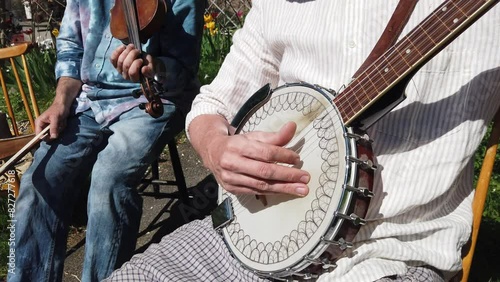 A musician plays the banjo accompanied by a violinist during a sunny day.