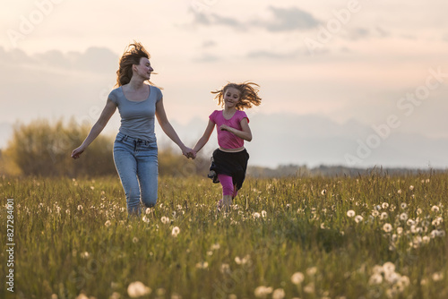 Mother and her little daughter running in the meadow into the sunset light.