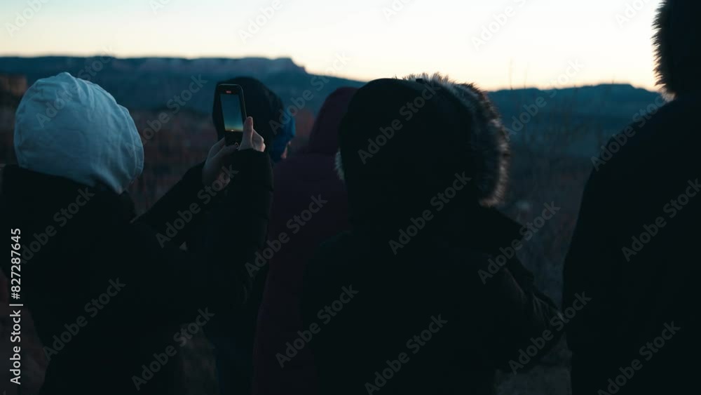 Shot of group of people, one holding a phone, waiting for a sunrise in chilly weather. Shot of group of people, one holding a phone, waiting for a sunrise in chilly weather.
