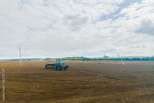 Spring autumn season countryside works.Harvesting farming wheat.Agricultural vehicle machine tractor is working on plowed field on sunny daytime.
