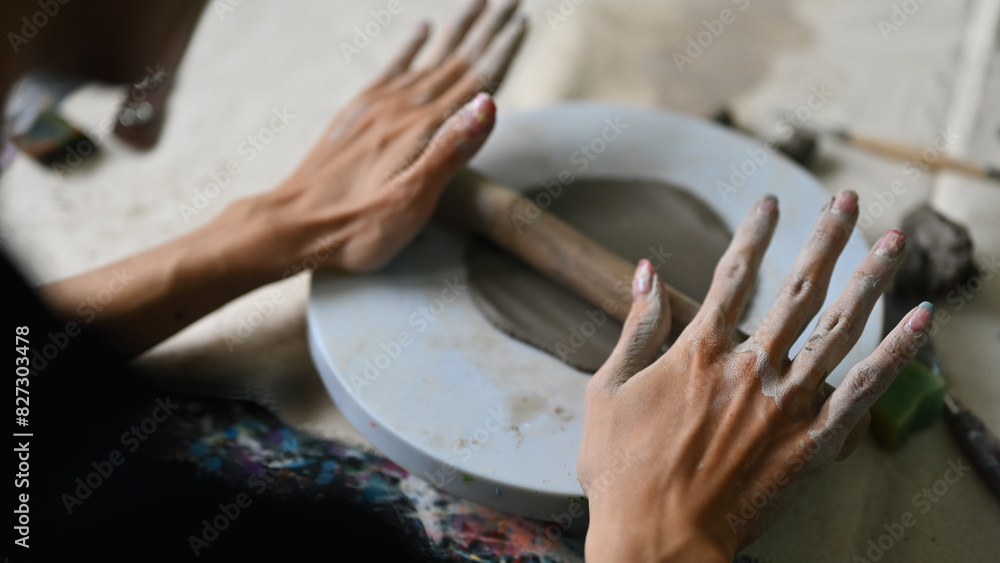 Close-up over-shoulder image of Young potter rolling out clay, Skillful Young artisan at work, rolling clay with a rolling pin Close-up over-shoulder image of Young potter rolling out clay, Skillful Young artisan at work, rolling clay with a rolling pin