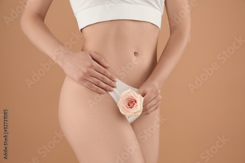 Gynecology. Woman in underwear with rose flower on beige background, closeup