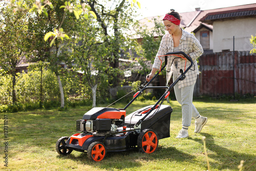 Obraz na plátně Smiling woman cutting green grass with lawn mower in garden