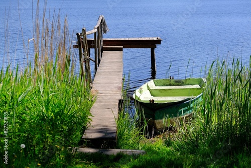 A wooden pier over a lake surrounded by forest in spring scenery. Wooden green boat standing on bank. Warmia and Masuria, Podlasie, Poland