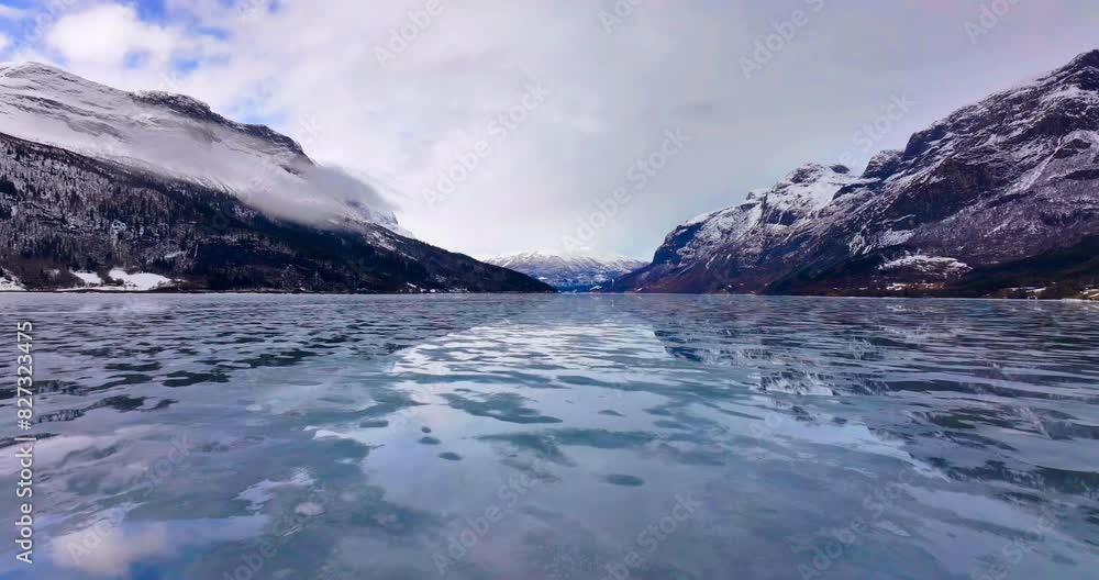 Drone shot of a reflective frozen lake with rocky mountains covered with snow in the background Drone shot of a reflective frozen lake with rocky mountains covered with snow in the background