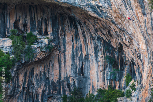 A rock wall with a person in a red t-shirt climbing it. The wall is made of limestone. Rodellar. Huesca. Spain.