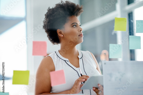 Black woman, thinking or brainstorming on glass wall, tablet or sticky note for schedule planning in office. Solution, research or designer in startup for ideas, problem solving or creative project