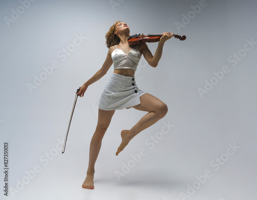 young blonde female musician plays the violin moving on one leg