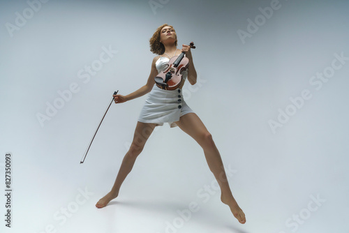 young blonde female musician plays the violin moving on one leg