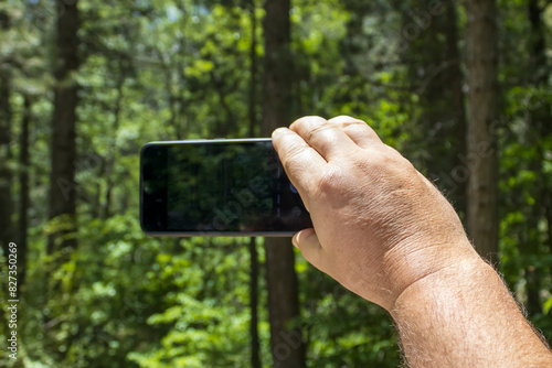 Man's hand taking pictures with smartphone in the forest 