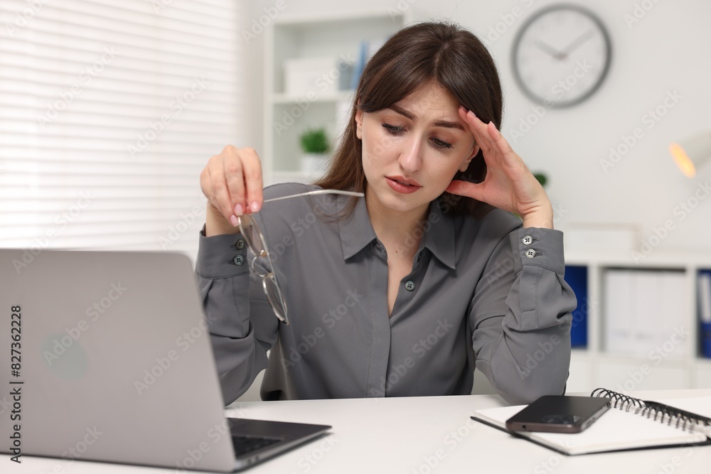 Overwhelmed woman sitting at table with laptop in office Overwhelmed woman sitting at table with laptop in office