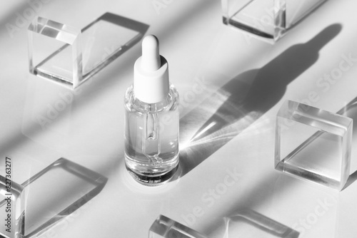 Serum cosmetic bottle mockup on acrylic transparent solid block pedestal on white background, shadow from sun, natural light from windows. Geometric stand, podium for cosmetics