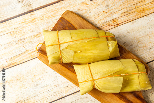 Obraz na plátně Two traditional Brazilian pamonhas wrapped in corn husks set on a wooden cutting board, showcasing a rustic and authentic Brazilian delicacy
