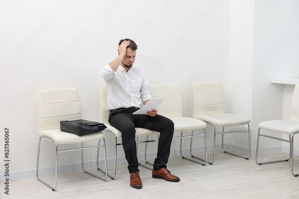 Man with sheet of paper waiting for job interview indoors Man with sheet of paper waiting for job interview indoors