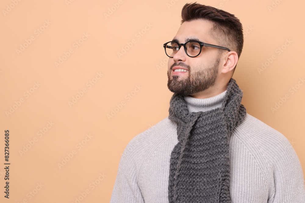 Fototapeta premium Smiling man in knitted scarf on beige background. Space for text