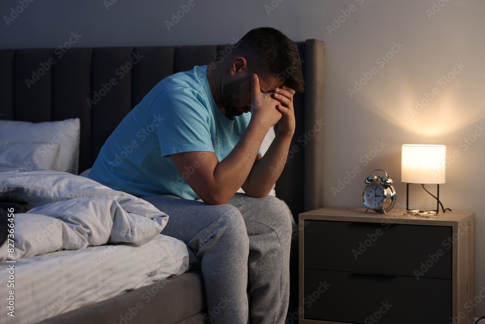 Fototapeta premium Man covering face with hands on bed indoors