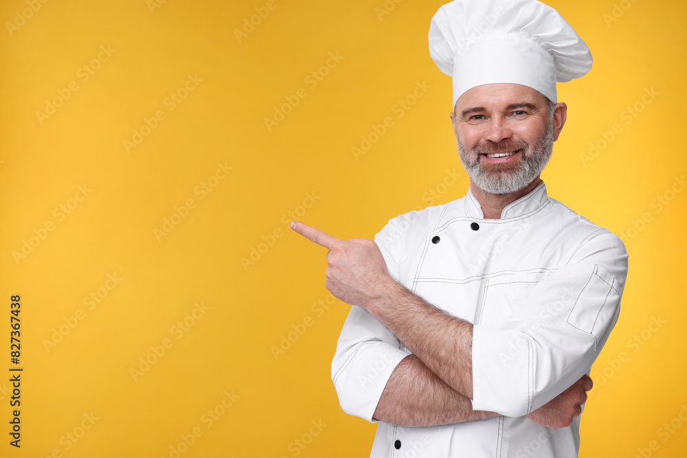 Happy chef in uniform pointing at something on orange background, space for text Happy chef in uniform pointing at something on orange background, space for text