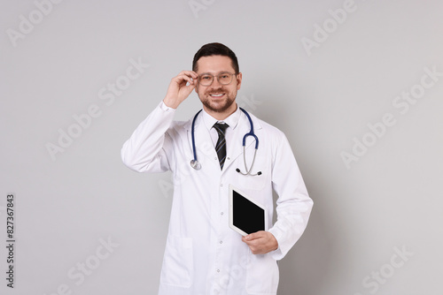 Portrait of smiling doctor with tablet on light grey background
