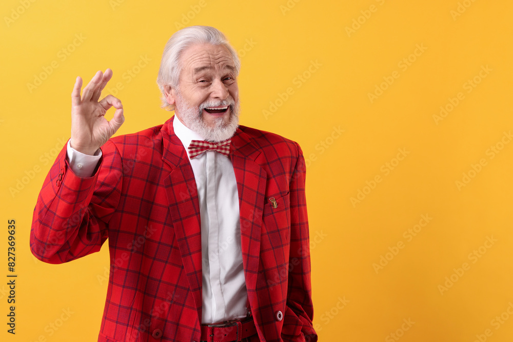 Portrait of grandpa with stylish red suit and bowtie showing ok gesture on yellow background, space for text