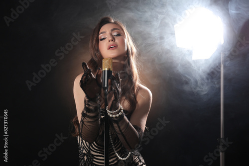 Beautiful young woman with microphone singing on dark background with smoke © New Africa