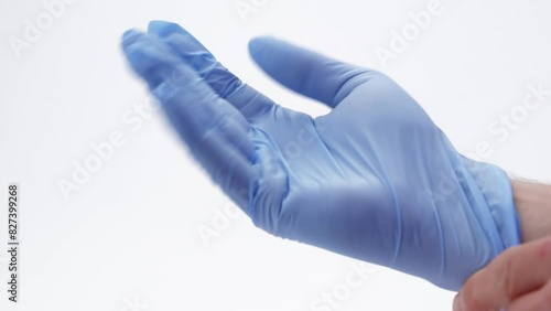 Caucasian male hand in a blue latex surgical glove bends fingers to achieve a better fit, filmed against a white background.

