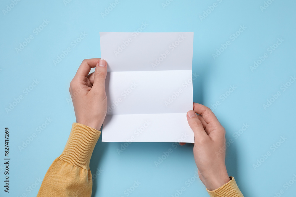 Woman with blank sheet of paper at light blue table, top view. Space for text Woman with blank sheet of paper at light blue table, top view. Space for text