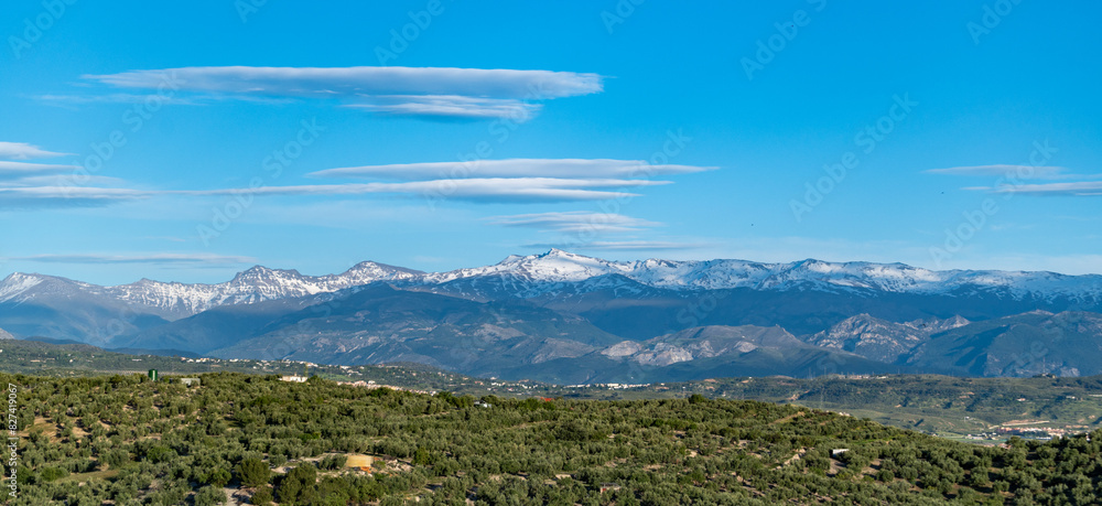 Huge lenticular clouds over the snowy peaks of the Sierra Nevada in Granada (Spain) at sunset Huge lenticular clouds over the snowy peaks of the Sierra Nevada in Granada (Spain) at sunset