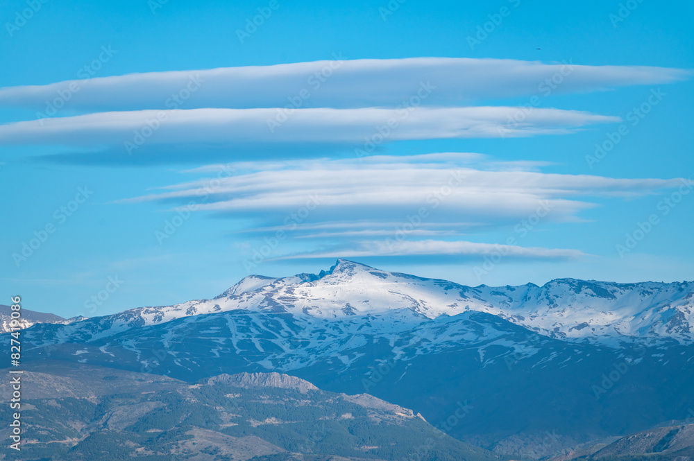 Huge lenticular clouds over the snowy peaks of the Sierra Nevada in Granada (Spain) at sunset Huge lenticular clouds over the snowy peaks of the Sierra Nevada in Granada (Spain) at sunset