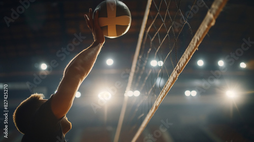 A volleyball player spikes the ball over the net in a well-lit indoor court during a match. photo