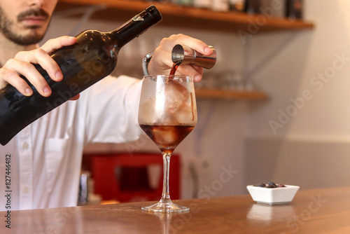 Unrecognizable waiter preparing a cocktail at a bar, pouring alcohol into the glass, with blueberries next to