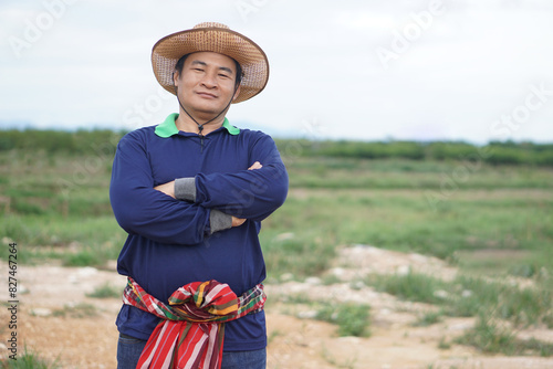 Handsome Asian man farmer stands at agricultural land, wears hat, Thai loincloth on waist, cross arms on chest, feels confident. Concept, agriculture occupation. 