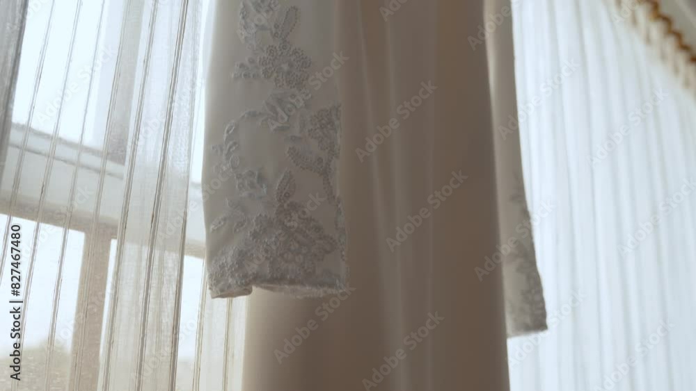 White wedding gown hanging from a white hanger by the window. close up 60fps White wedding gown hanging from a white hanger by the window. close up 60fps