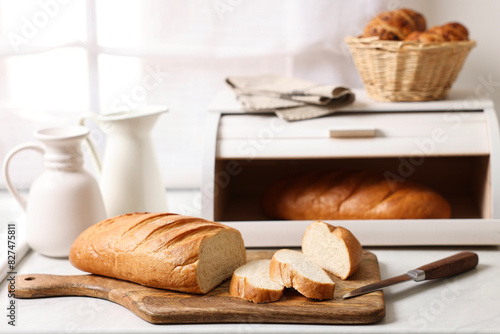 Wooden bread basket with freshly baked loaves on white marble table in kitchen photo