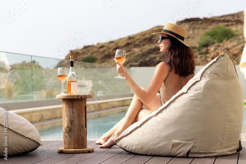 Woman in straw hat and sunglasses drinking wine near the pool