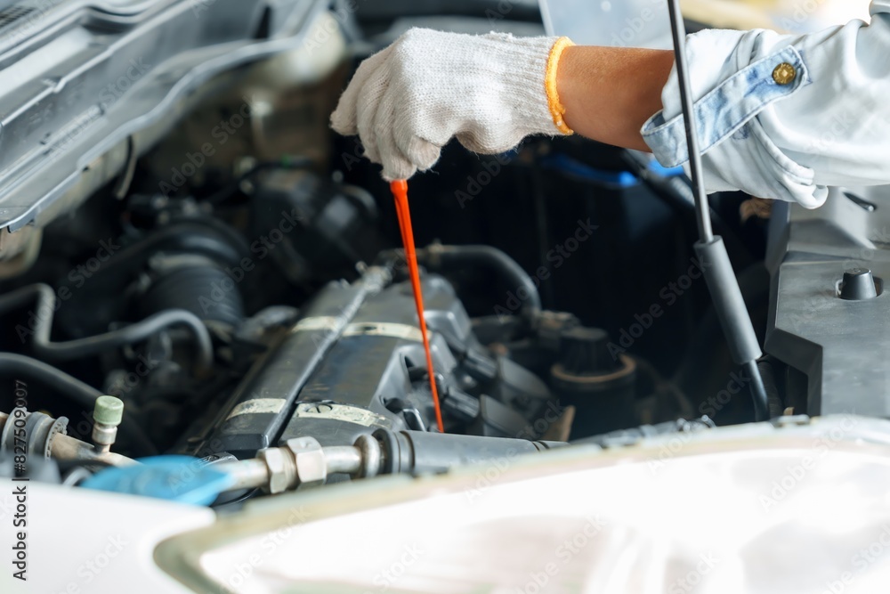 Gloved mechanic hand checking engine oil dipstick in a car engine, with laptop on hood. Represents routine maintenance and diagnostics in a small garage. Focus on precision and technical expertise. Gloved mechanic hand checking engine oil dipstick in a car engine, with laptop on hood. Represents routine maintenance and diagnostics in a small garage. Focus on precision and technical expertise.