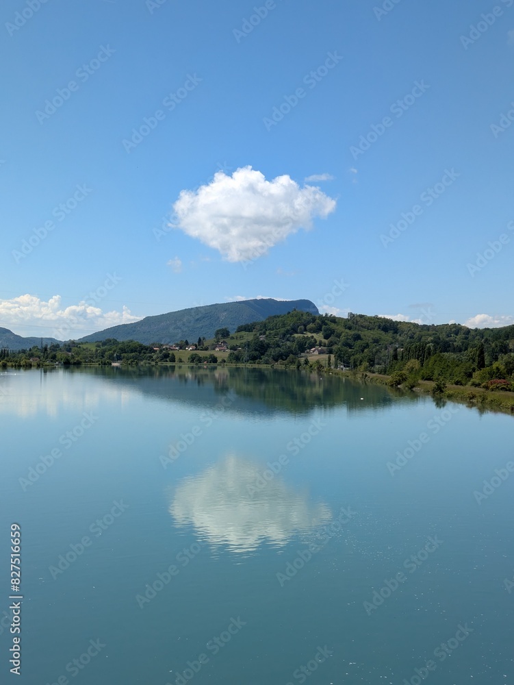 Isolated fluffy cloud above hill reflecting in Rhone river channel, Belley, France