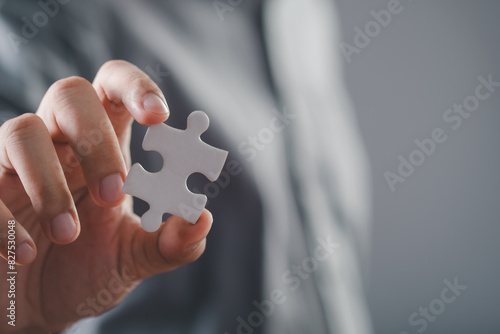 businessman hand holding puzzle piece with gray background. Jigsaw puzzle team work concept. one part of whole. symbol of association and connection. business strategy.