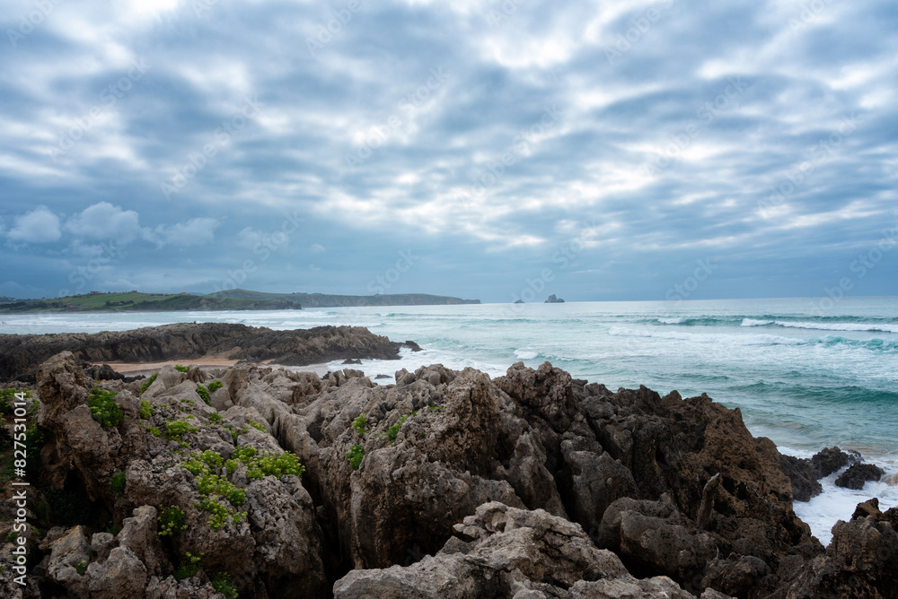 A rocky shoreline with a cloudy sky in the background. The ocean is visible in the distance, Natural Park of the Dunes of Liencres, Cantabria, Spain