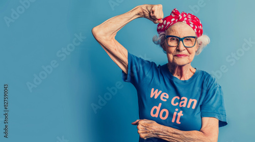Confident elderly woman in a we can do it shirt flexing arm muscles on blue background photo