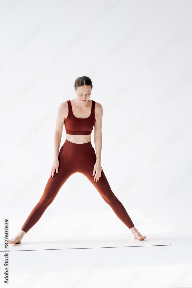 A slender woman in a brown sports uniform does stretching with difficulty on a white background A slender woman in a brown sports uniform does stretching with difficulty on a white background