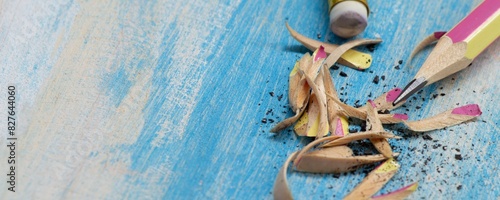 A broken yellow pencil with an eraser and pencil shavings on a blue wooden background.