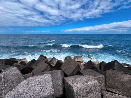 Turquoise blue sea water with white foam on wave splashes. Water washes black volcanic square stone blocks. Tenerife, Puerto de la Cruz