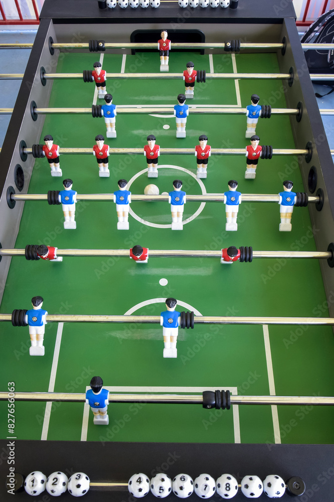 Classic Foosball Table Game With Players in Red and Blue Jerseys During Daytime Indoor Match. Close-up view of foosball table featuring red and blue jersey players positioned for daytime indoor game. Classic Foosball Table Game With Players in Red and Blue Jerseys During Daytime Indoor Match. Close-up view of foosball table featuring red and blue jersey players positioned for daytime indoor game.
