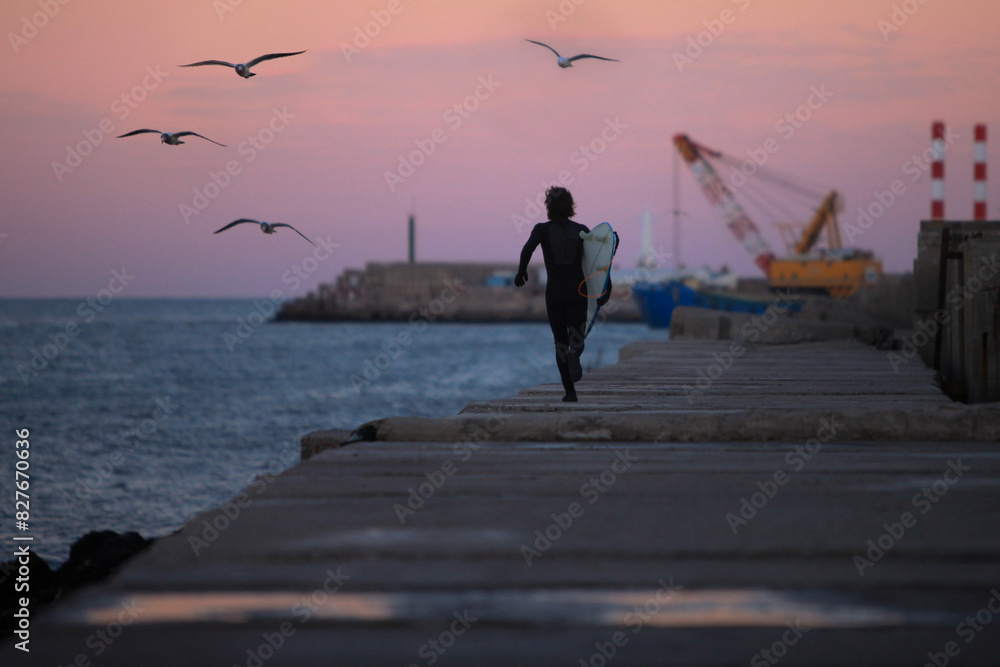 Fototapeta premium surfer running along pier just after sunset with port and ocean in background