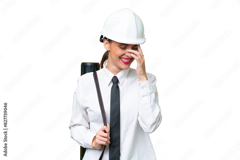 Young architect woman with helmet and holding blueprints over isolated background laughing Young architect woman with helmet and holding blueprints over isolated background laughing